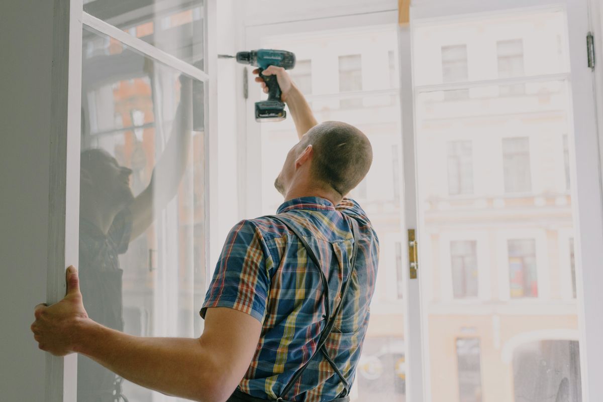 Installer fixing an aluminium window frame with a drill during replacement