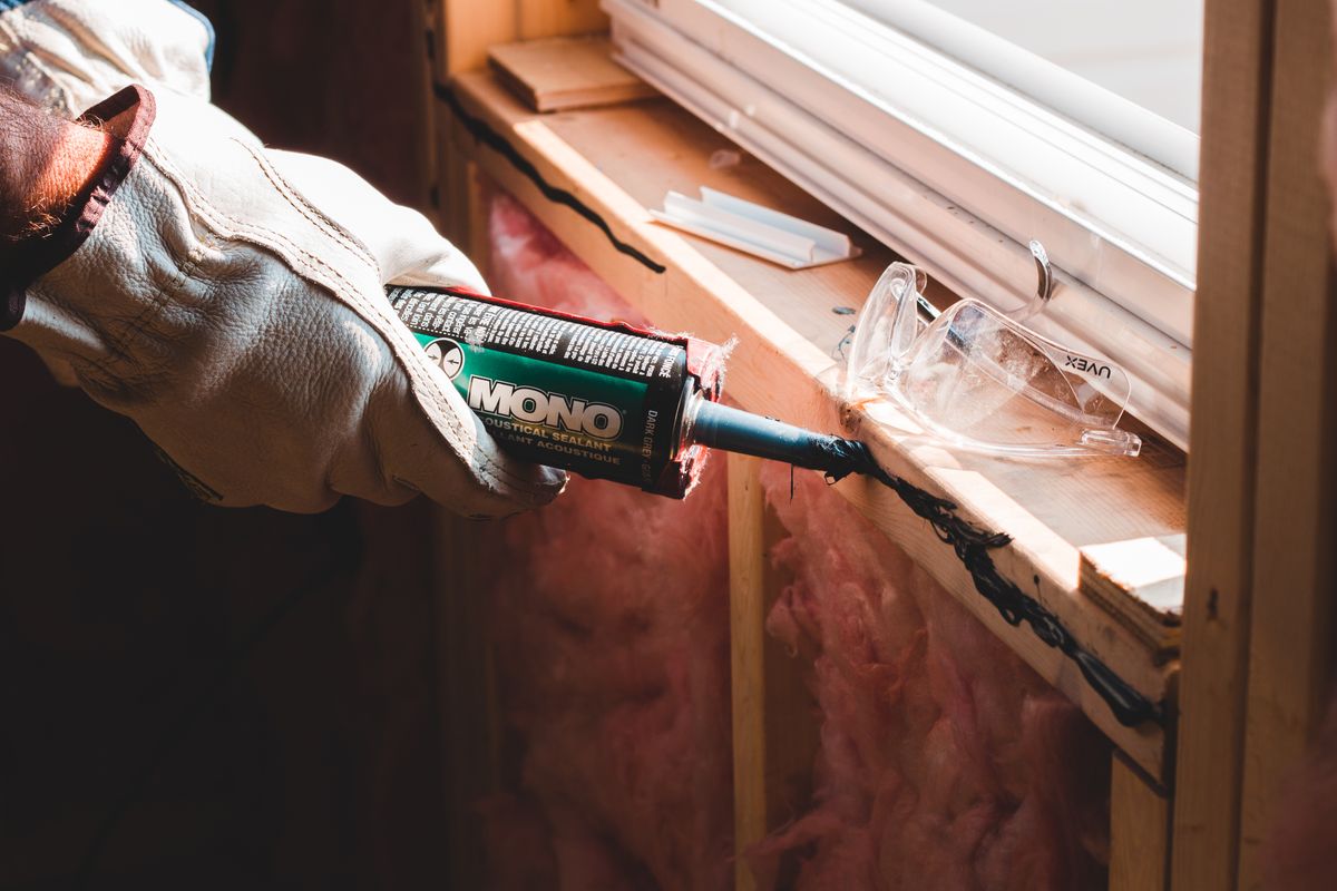 Technician applying acoustic sealant around a window opening during installation